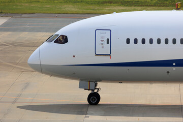Close-up view of a commercial airplane cockpit and nose section at an airport. A pilot is preparing for flight, representing the aviation and travel industry.