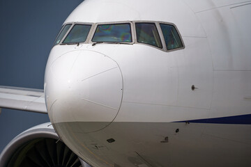 Close-up view of a commercial airplane cockpit and nose section at an airport. A pilot is preparing for flight, representing the aviation and travel industry.
