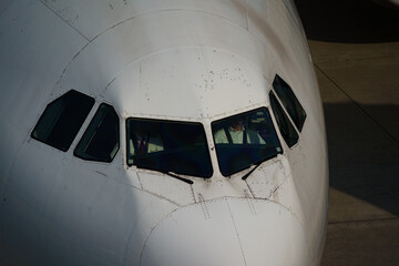 Close-up view of a commercial airplane cockpit and nose section at an airport. A pilot is preparing for flight, representing the aviation and travel industry.