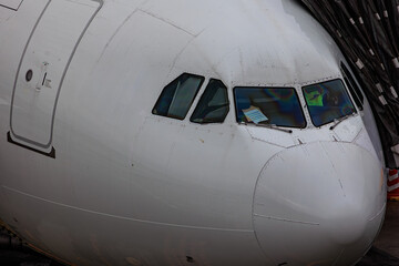 Close-up view of a commercial airplane cockpit and nose section at an airport. A pilot is preparing for flight, representing the aviation and travel industry.