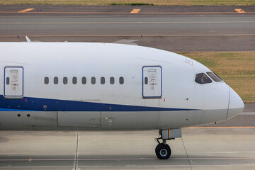 Close-up view of a commercial airplane cockpit and nose section at an airport. A pilot is preparing for flight, representing the aviation and travel industry.