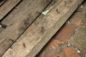 Close up view of old wooden beams with rusty nails and brick flooring