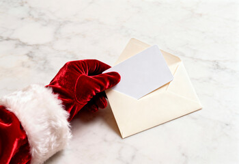 Santa glove sliding blank card into cream envelope on marble