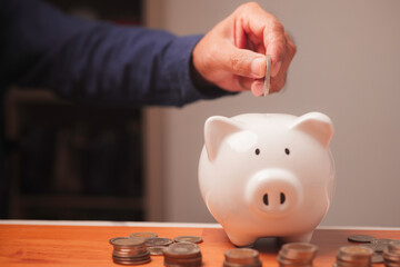 A hand placing a coin into a white piggy bank represents saving money, financial planning, and...