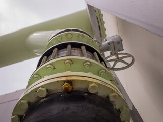Close-up of industrial water pipe joint with bolted flange, flexible connector, and valve actuator. Visible rust and wear indicate active use in a utility system.