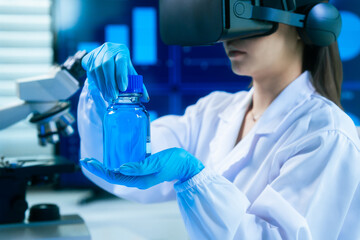 An Asian female scientist in a modern lab interacts with 3D holographic data using VR/MR headset,...