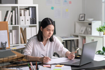 Young Asian Businesswoman looking stressed while talking on the phone, Young businesswoman working at office feels overworked and burnout