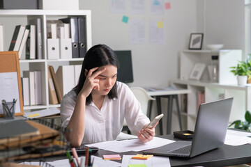 Young Asian Businesswoman looking stressed while talking on the phone, Young businesswoman working at office feels overworked and burnout