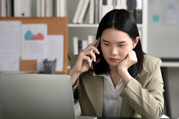 Young Asian Businesswoman looking stressed while talking on the phone, Young businesswoman working at office feels overworked and burnout