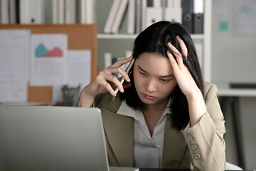 Young Asian Businesswoman looking stressed while talking on the phone, Young businesswoman working at office feels overworked and burnout