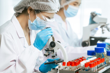 Two focused Asian scientists work in a bright laboratory with microscope, test tubes, and chemical solutions, performing biological, pharmaceutical, and analytical research with scientific precision