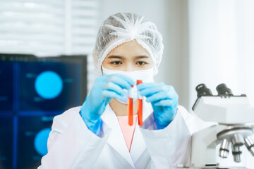 An Asian female scientist carefully analyzes microscopic samples and chemical solutions in a modern...