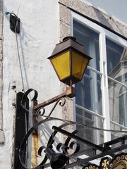 Rusty yellow lantern mounted on old white wall with window in daylight
