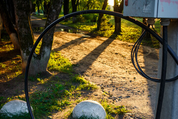 A winding black cable forms an arc in the foreground, framing a sun-drenched dirt path in a park with trees and long shadows
