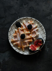 Belgian waffles served with figs and blackberries on a dark background, top view