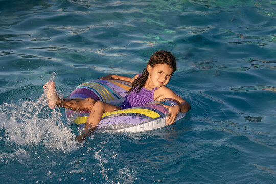 Smiling child girl sits on summer pool float and splashes water with her feet