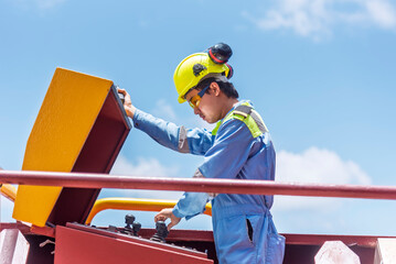Navigational officer in blue and yellow uniform on the deck of a large merchant ship near mooring winch control station. 