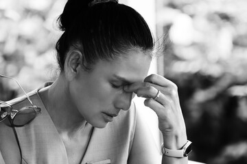 Black and white portrait of an adult woman with her hand on her forehead, expressing worry, stress, or a headache. A depiction of deep thought, anxiety, or discomfort.