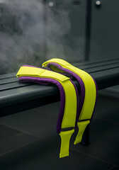Yellow and purple weightlifting straps resting on a dark bench in a locker room. Athletes' equipment in a smoky locker room setting.
