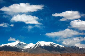 Fototapeta premium Snow-capped mountains under a clear blue sky with scattered clouds