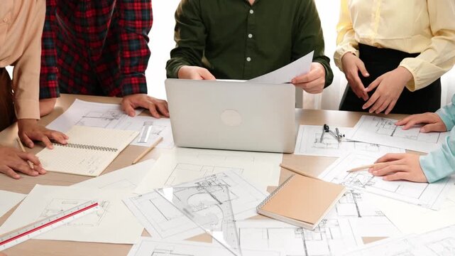 Smart architect and safety engineer discussion about building plan on table with architectural document, measurement tools and wooden block scatter around at modern office. Closeup. Delineation.