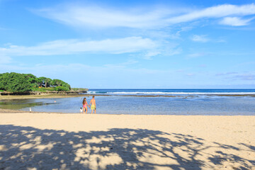 Couple walking on a beach with a clear blue sky above them