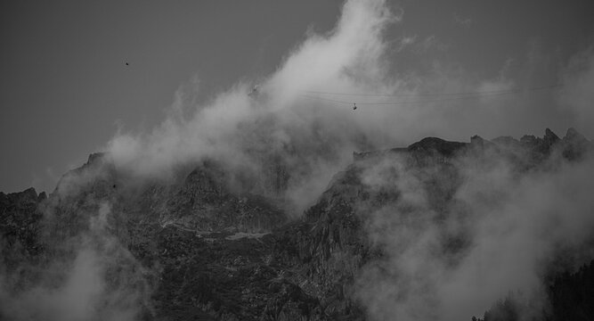 High resolution close up image of the Mont Blanc Alps covered with clouds with a distant cable cart climbing it- France