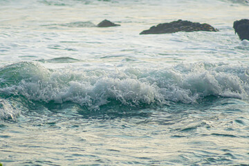 White Foam Wave Rolling Over the Ocean with Rocks in the Background