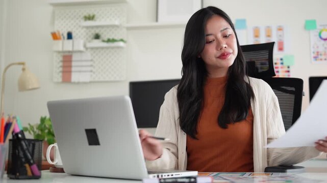 Professional UX UI designer working on a laptop while reviewing wireframes and design mockups in a modern office.