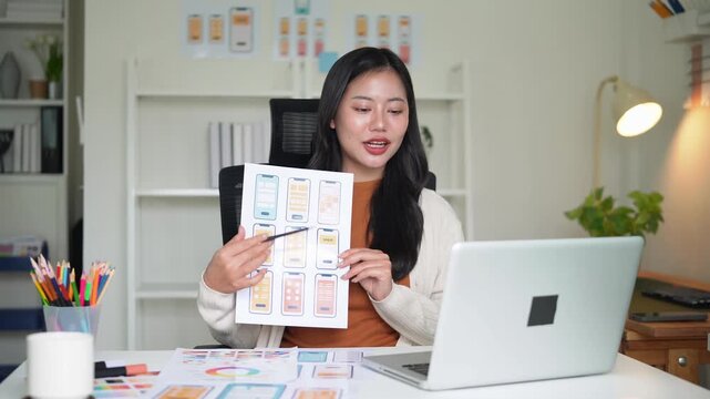 Smiling UX UI designer presenting mobile app wireframes during an online meeting in a modern workspace.