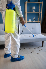 Pest control exterminating roaches. Male exterminator in protective suit spraying insecticide on...