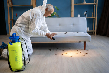 Pest control contractor wearing white protective suit using flashlight while working in the flat