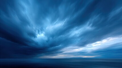 A dramatic sky filled with swirling blue and gray clouds above a calm ocean, creating a moody and atmospheric seascape.