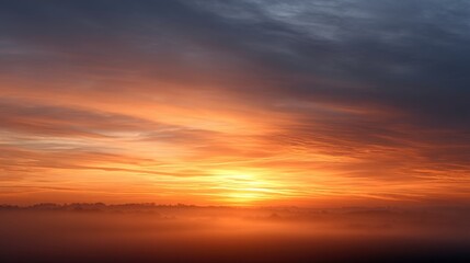 A breathtaking sunset casts vibrant orange and yellow hues across the sky, blending with soft clouds and misty landscapes for a serene natural scene.