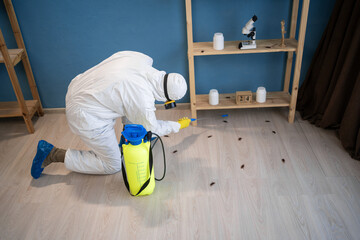 Male exterminator killing cockroaches in house. Pest control worker in protective suit and...