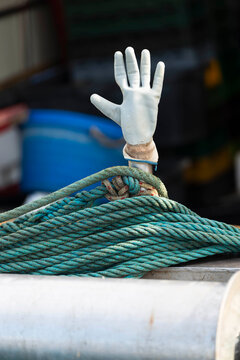 Weisser Gummihandschuh steckt auf einem Stab oberhalb eines t&uuml;rkisen Tau auf einem Fischerboot im Hafen von Cres, Kroatien