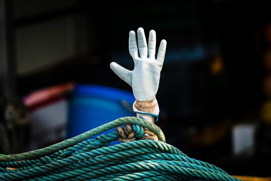 Weisser Gummihandschuh steckt auf einem Stab oberhalb eines t&uuml;rkisen Tau auf einem Fischerboot im Hafen von Cres, Kroatien