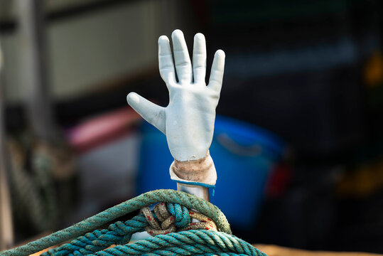 Weisser Gummihandschuh steckt auf einem Stab oberhalb eines t&uuml;rkisen Tau auf einem Fischerboot im Hafen von Cres, Kroatien