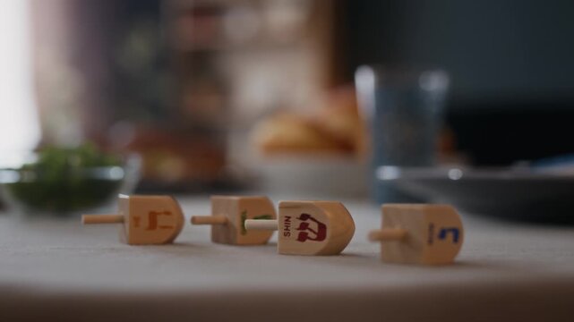 No people close up shot of four dreidels with engraved letters of Hebrew alphabet lying on table set for Hanukkah celebration in modern Jewish apartment