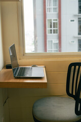 Laptop on Wooden Desk by Window Overlooking City Buildings Natural Light Illuminates Workspace