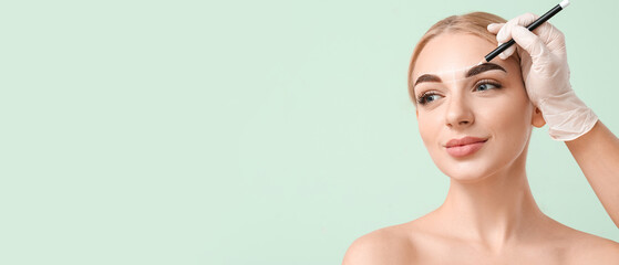 Young woman undergoing eyebrow correction procedure on color background