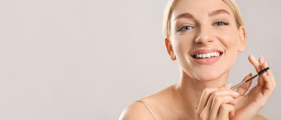 Young woman correcting her eyebrows on grey background
