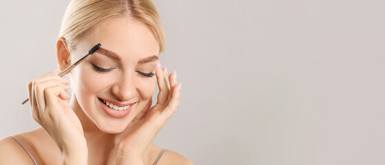 Young woman correcting her eyebrows on grey background