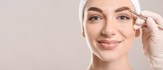 Young woman undergoing eyebrow correction procedure on grey background