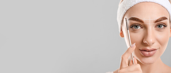 Young woman correcting her eyebrows against grey background