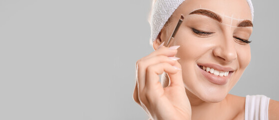 Young woman correcting her eyebrows against grey background