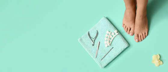 Feet of young woman, flower and set for pedicure on turquoise background