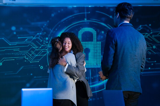 Diverse cybersecurity team celebrating a successful project with hugs and handshakes in a modern office.