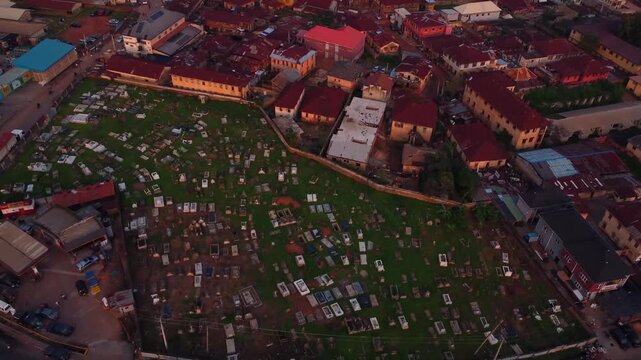 Drone video captures a solemn cemetery at dusk, with rows of graves and tombstones casting shadow under dim light at countryside, Nigeria. Peaceful aerial footage evokes a reflective mood of deceased.