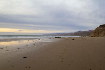 Cloudy beach at low tide with mountain shoreline at sunset